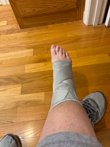 Customer wearing the grey adjustable Premium Bamboo Ankle Support on their foot while sitting on a wooden floor.