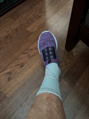 Customer's foot wearing a light-colored Premium Bamboo Ankle Support sleeve inside a purple shoe on a wooden floor.