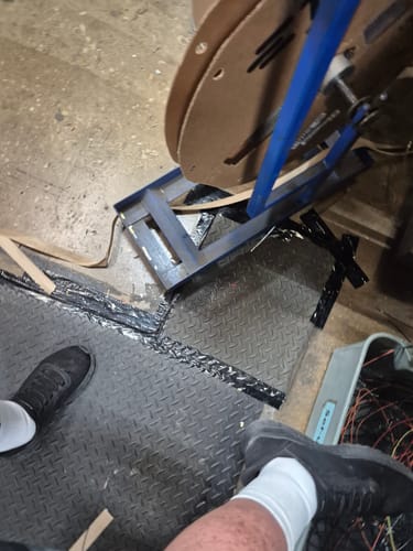 Reviewer's view of their feet, showing one wearing the black Premium Bamboo Ankle Support over a sock in a workshop.