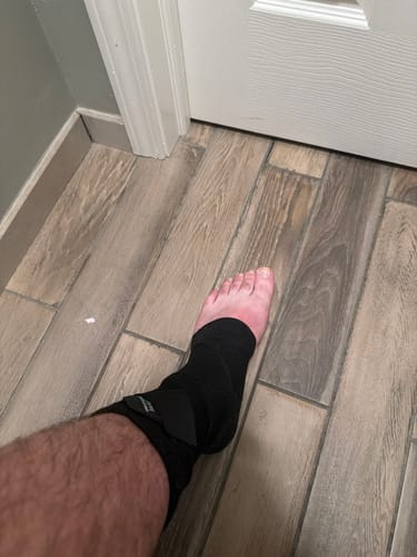 A customer wearing the black Premium Bamboo Ankle Support on their foot while standing indoors.