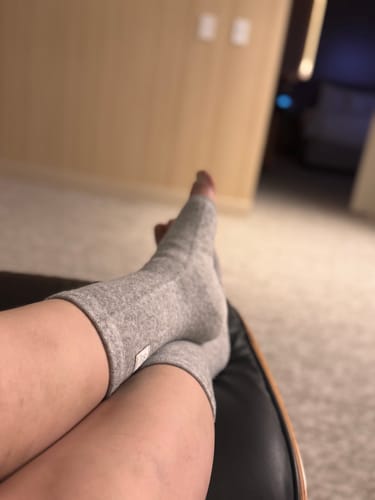Reviewer relaxing with their feet crossed on a chair, wearing the grey Bamboo Footsleeves.