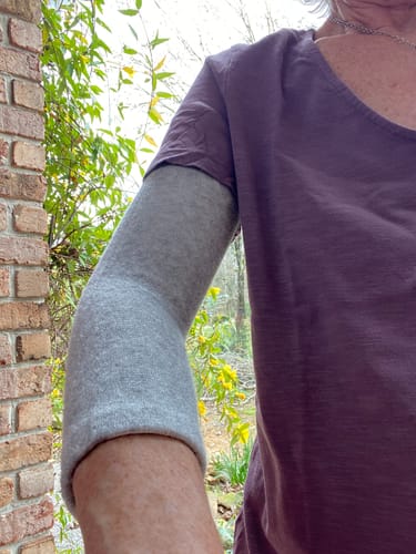 Customer wearing a grey compression elbow sleeve on their arm, with the sleeve pulled up to their bicep.