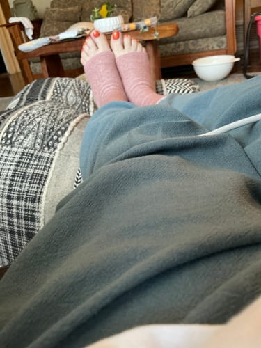 Customer's feet wearing pink Premium Anti-Fatigue Bamboo Footsleeves while resting on a couch.