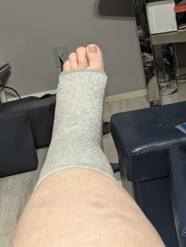 Customer resting with their foot up, wearing the open-toed grey Bamboo Footsleeve.