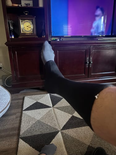 Reviewer relaxing at home with their feet up, wearing the black and grey Premium Anti-Fatigue Bamboo Footsleeves.