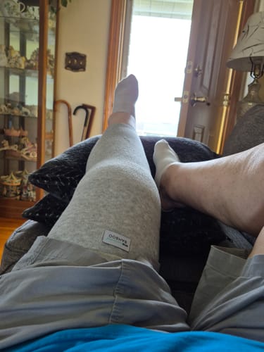 Customer resting with their leg propped up while wearing the light grey Premium Bamboo Leg Sleeve.