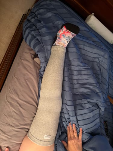 image 2 out of 2: Reviewer's leg in a grey Premium Bamboo Leg Sleeve, shown resting on a bed with a blue comforter.