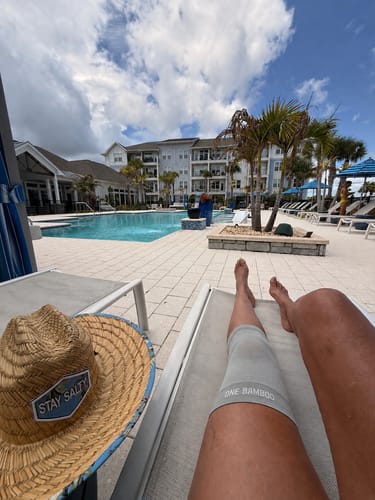 Customer wearing the light grey Premium Bamboo Knee Sleeve while relaxing on a lounge chair by a pool.