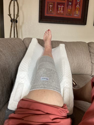 Reviewer resting on a couch with their leg elevated on a pillow, wearing the grey Bamboo Knee Sleeve.
