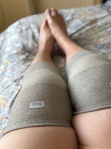 Reviewer wearing two gray Premium Bamboo Knee Sleeves on both knees while relaxing on a bed.