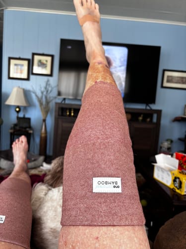 Customer wearing two reddish Premium Bamboo Knee Sleeves on their legs while resting at home.