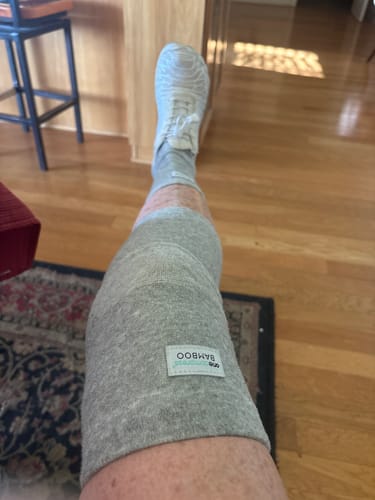 Customer relaxing indoors while wearing the grey Premium Bamboo Knee Sleeve on their leg.