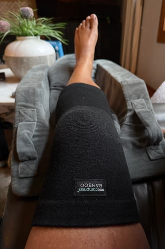 Reviewer wearing the black Premium Bamboo Knee Sleeve while resting with their leg elevated on a pillow.