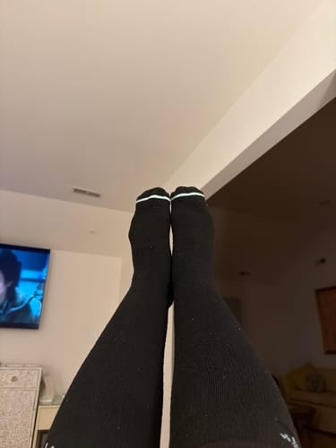 Customer's feet wearing black Premium Bamboo Compression Socks with white stripes at the top, shown in a home setting.