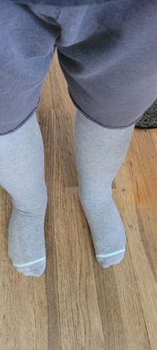 Reviewer's view of their legs while wearing the grey bamboo compression socks on a wooden floor.
