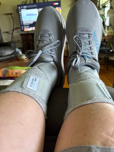 Customer wearing the Premium Bamboo Ankle Support on both ankles with grey running shoes while resting.
