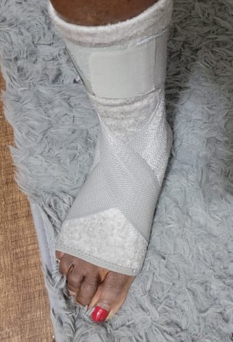 Customer's foot wearing a light grey Premium Bamboo Ankle Support, resting on a fuzzy grey rug.