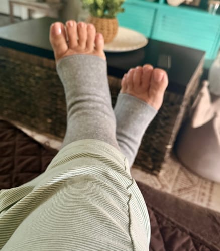 Customer relaxing with feet up, wearing the grey toeless Premium Anti-Fatigue Bamboo Footsleeves.