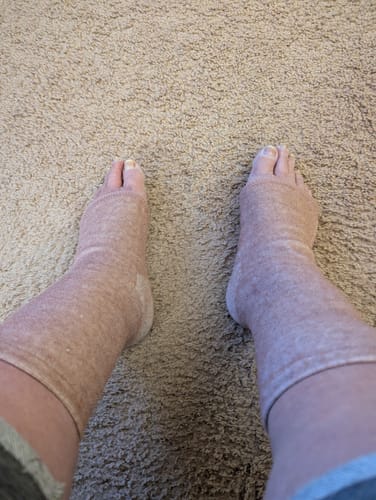 Customer's feet in comfortable, light brown Premium Anti-Fatigue Bamboo Footsleeves while standing on a carpet.
