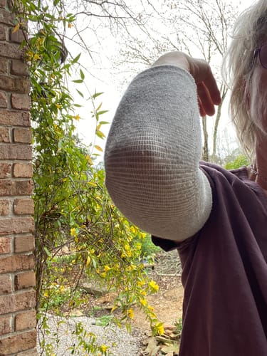 image 2 out of 2: Close-up of a customer's bent elbow, showing the flexible, textured weave of the grey compression sleeve.