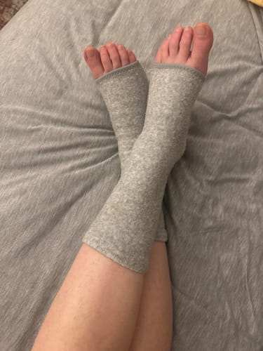 Reviewer's feet crossed while resting in bed and wearing the grey open-toed Bamboo Footsleeves.