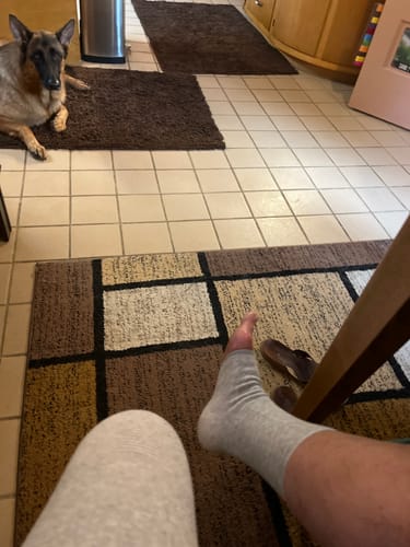 Customer's first-person view of their foot in a grey open-toed Anti-Fatigue Footsleeve while relaxing at home.
