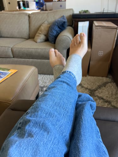 Customer's feet wearing light gray Premium Anti-Fatigue Bamboo Footsleeves while resting on a sofa.