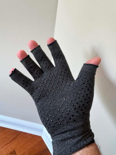 Reviewer showing their hand wearing a dark grey, fingerless Onecompress™ Glove with dotted grip.