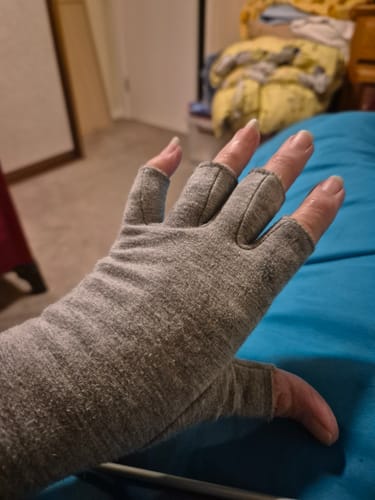 A reviewer's hand wearing the grey, open-fingertip Premium Onecompress™ Gloves in a bedroom setting.