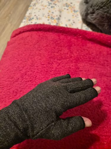 Reviewer's hand wearing a dark grey, fingerless Premium Onecompress™ Glove while resting on a red blanket.