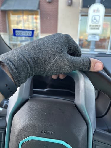 Customer wearing a grey Onecompress™ Glove while holding a car's steering wheel.