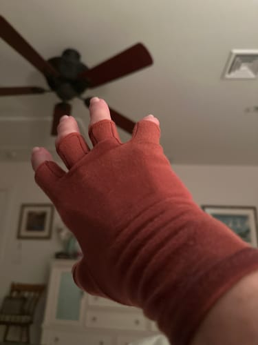 A reviewer's hand wearing the reddish Onecompress™ Gloves, showing the open-finger design.