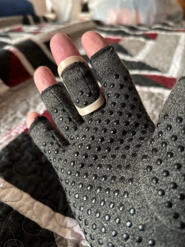 A reviewer's hand wearing the grey, textured Onecompress™ Glove with a plastic finger splint over the middle finger for arthritis.