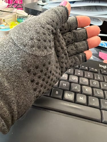 Close-up of a reviewer's hand in a grey, dotted Onecompress™ Glove with open fingertips, resting by a keyboard.