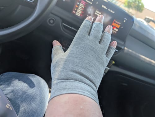 Customer's hand wearing a grey open-finger Premium Onecompress™ Glove inside a car.