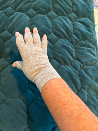Reviewer's hand wearing a light grey, fingerless Premium Onecompress™ Glove against a green quilted surface.