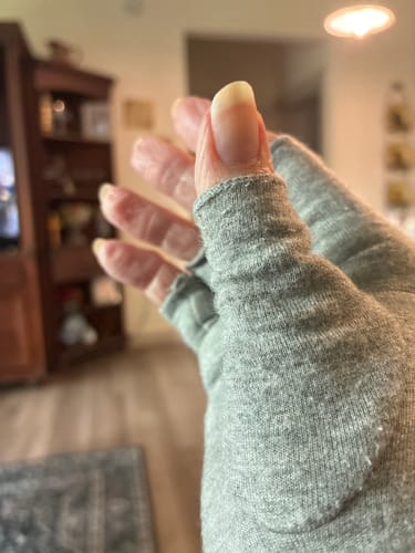 Close-up of a customer's hand wearing the grey, open-finger Premium Onecompress™ Gloves indoors.