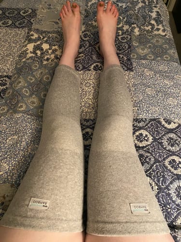 Customer's gray Premium Bamboo Leg Sleeves worn on both legs while resting on a patterned bedspread.