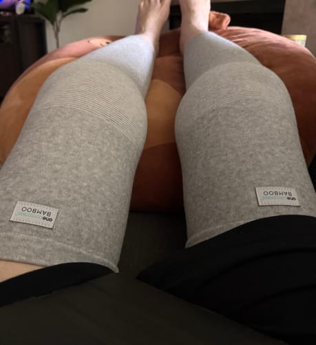 Reviewer wearing a pair of grey Premium Bamboo Leg Sleeves while resting with their legs propped up on a cushion.