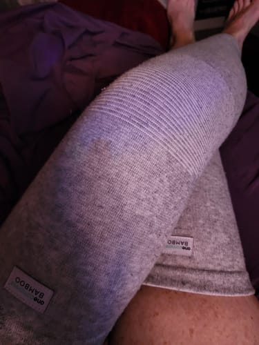 Customer's legs wearing two gray Premium Bamboo Leg Sleeves, showing the soft fabric texture and product branding labels.