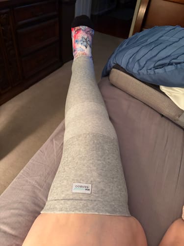 Customer wearing the grey, full-length Premium Bamboo Leg Sleeve while relaxing on a bed.