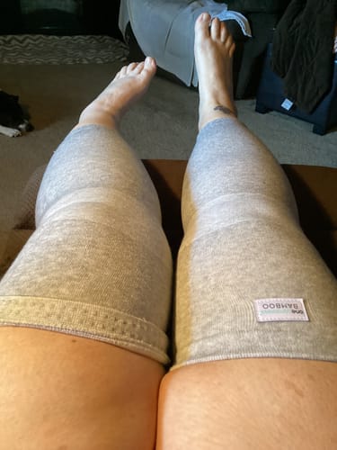 Reviewer relaxing with their feet up, wearing two grey Premium Bamboo Leg Sleeves that cover from thigh to ankle.
