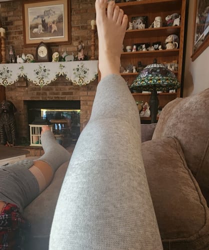 Customer resting on a couch wearing the grey Premium Bamboo Leg Sleeve on one leg while the other leg is bandaged.