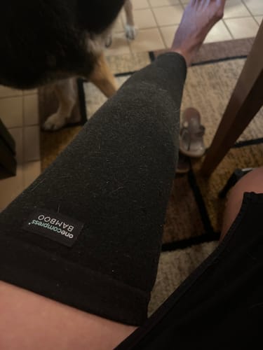 Customer wearing the dark Premium Bamboo Leg Sleeve on their lower leg while sitting indoors.