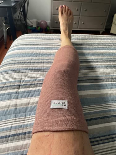 Customer wearing the pink bamboo knee sleeve on their leg while resting in bed.