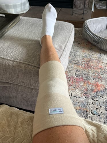 Customer resting their leg on an ottoman while wearing the light-colored Premium Bamboo Knee Sleeve.