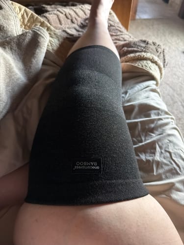 Customer wearing the dark Premium Bamboo Knee Sleeve on their leg while resting in bed.