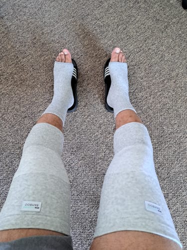 Reviewer wearing two light gray Premium Bamboo Knee Sleeves and matching ankle supports while sitting.