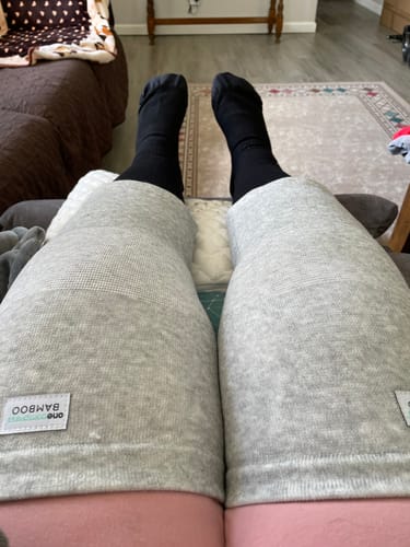 Reviewer wearing two light gray Premium Bamboo Knee Sleeves while resting their legs in a living room.