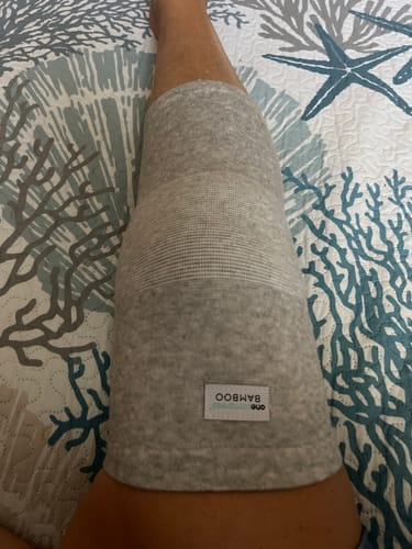Customer wearing the grey Premium Bamboo Knee Sleeve on their knee while resting on a patterned bedspread.